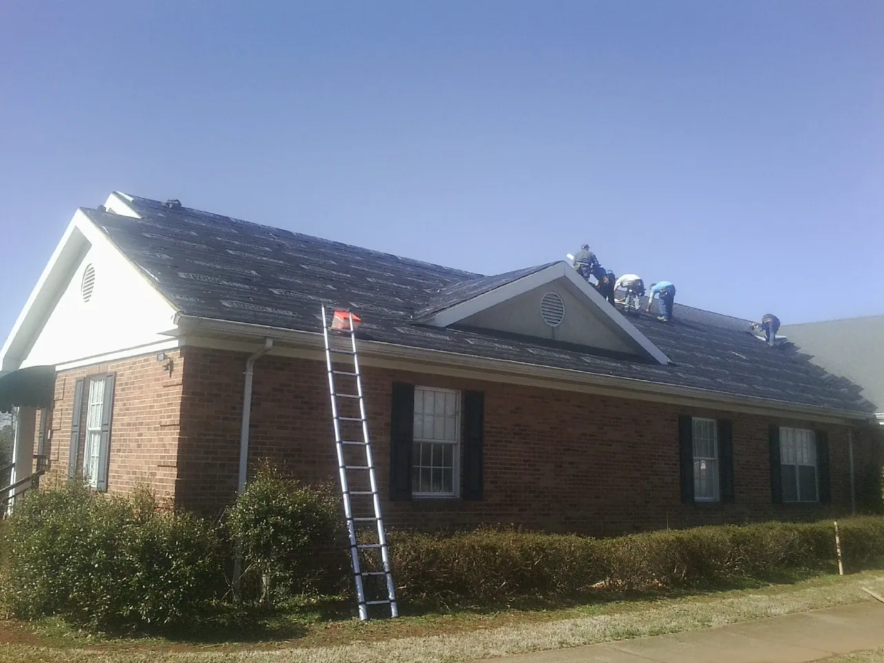 Crew tearing shingles off a brick ranch roof with a ladder set — Emergency Roof Repair work by our crew in Garden Valley