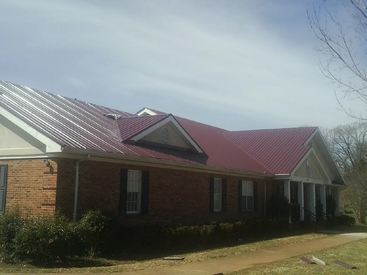 Red metal roof with gabled entries on a long brick building, from a Hail Damage Roof Repair job in Garden Valley